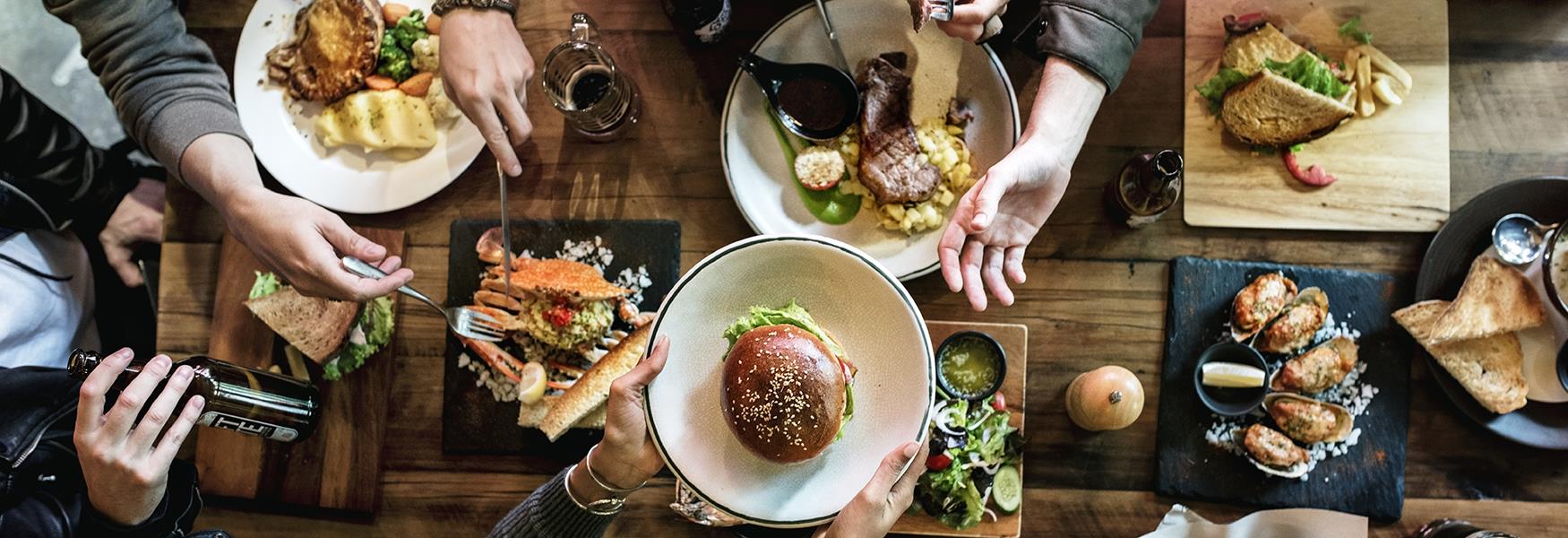 mange matretter på et bord og folk som sitter rundt bordet og spiser