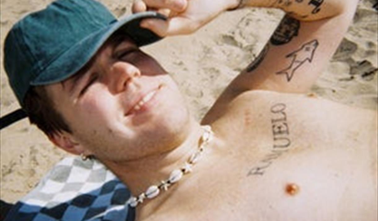 mann med ola caps i bar overkropp med tatoveringer