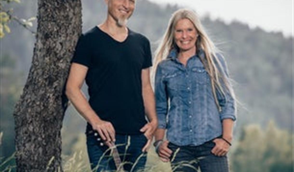 en dame med langt lyst hår ved siden av en mann stående mot et tre