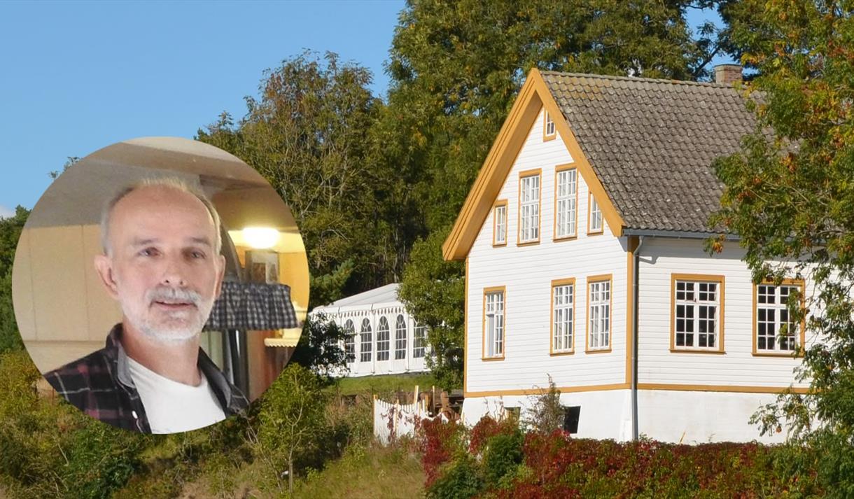 hvitt trehus med mørk gul farge rundt vinduene, en runding med et bilde av en mann