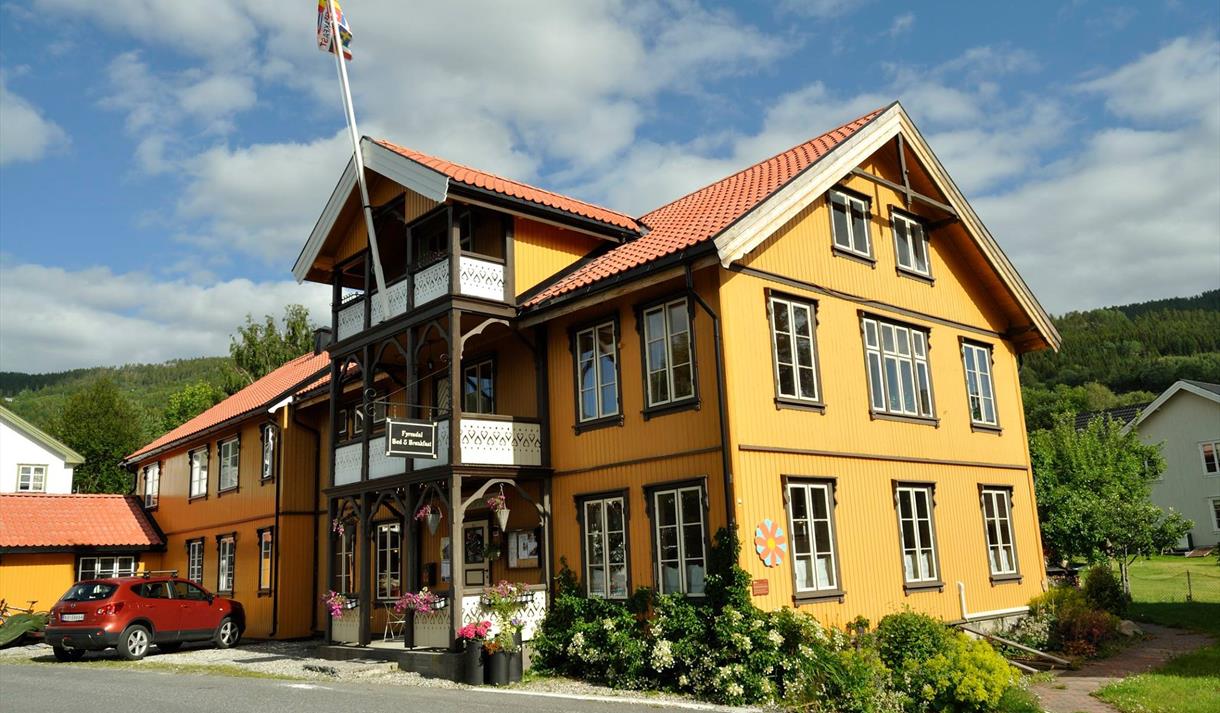 Fyresdal Bed og Breakfast på en solskinndag. Blomster rundt det gule huset.