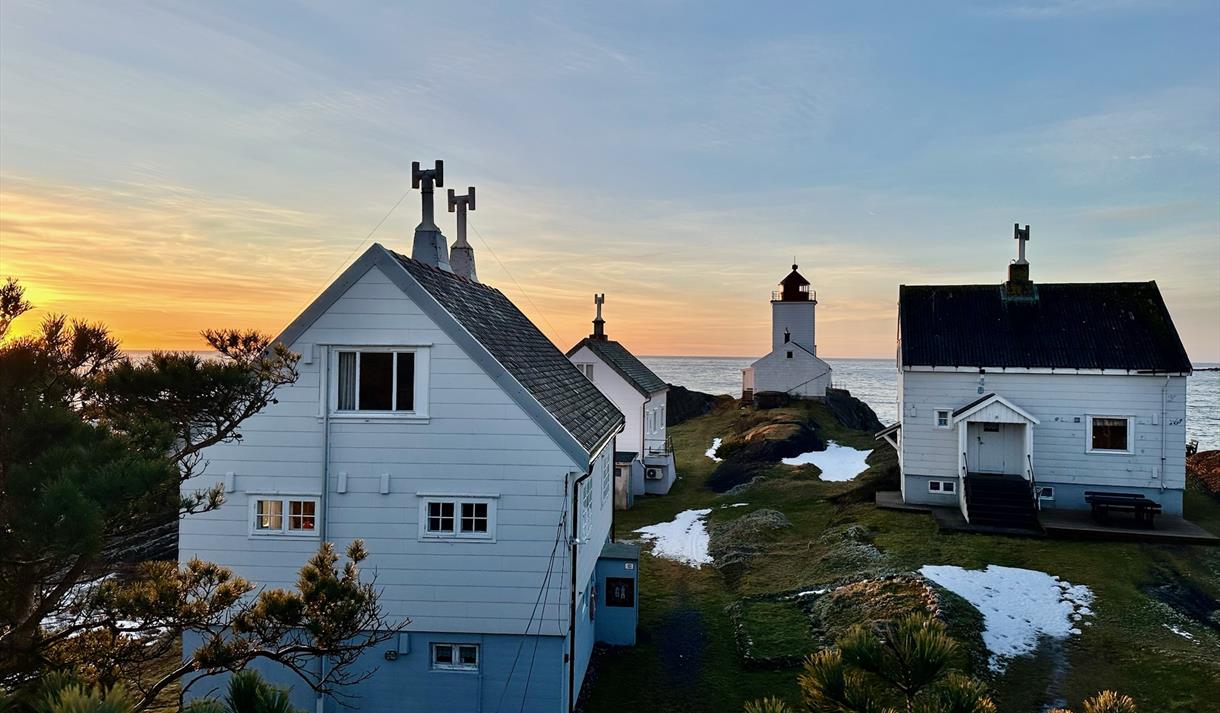 hvite hus med fyrhus i bakgrunn, gul oransje himmel
