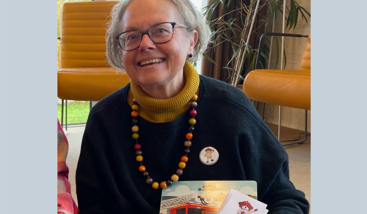 lyshåret dame med briller, sort genser og perlekjede i forskjellige farger