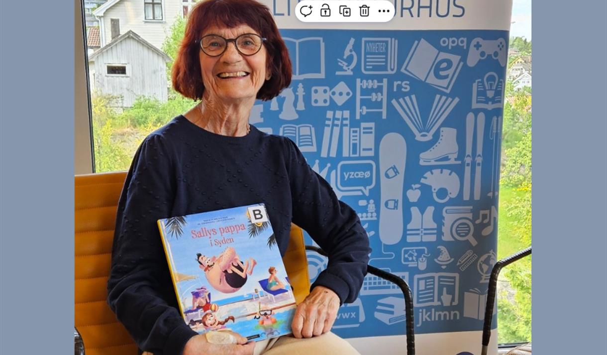bilde av blid dame med mørkt hår og briller med bok i hånda