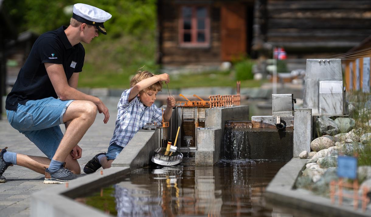 Slusevoktar og gutt slusar båtar i Telemarkskanalen på museet i Eidsborg.