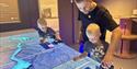 To born og ein vaksen ved spelbordet i Statkraft-utstillinga på Vest-Telemark museum Eidsborg.