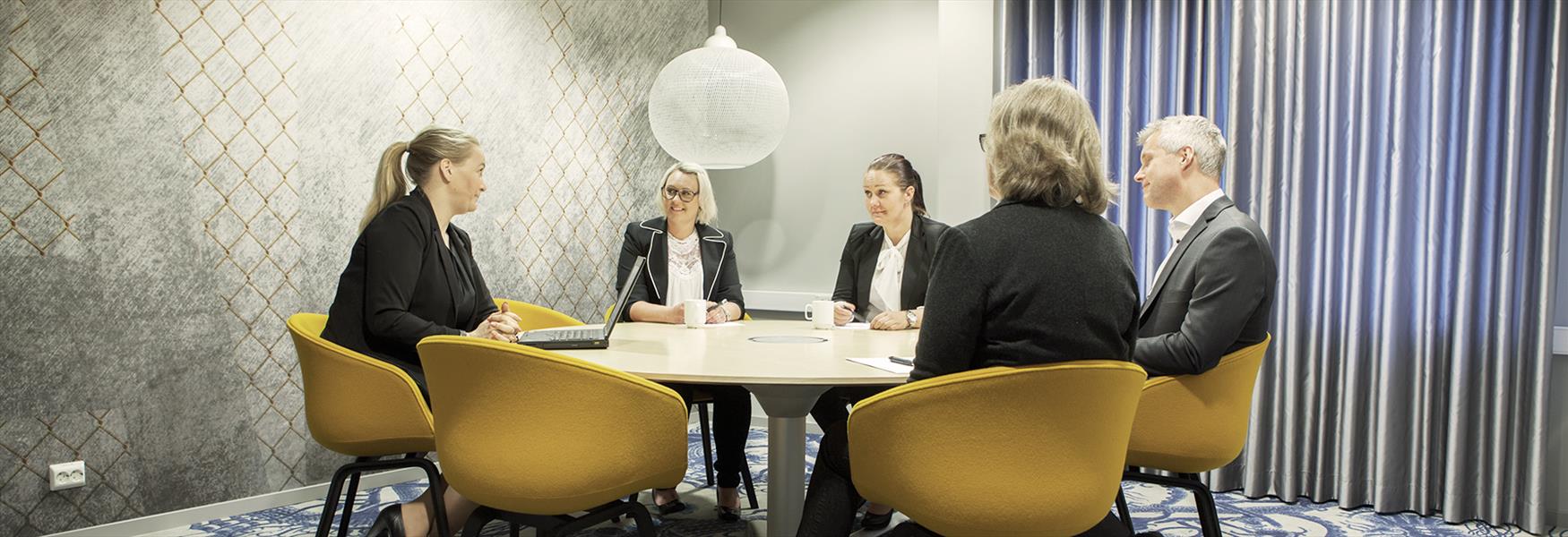 gruppe mennesker sitter rundt et bord på møterom