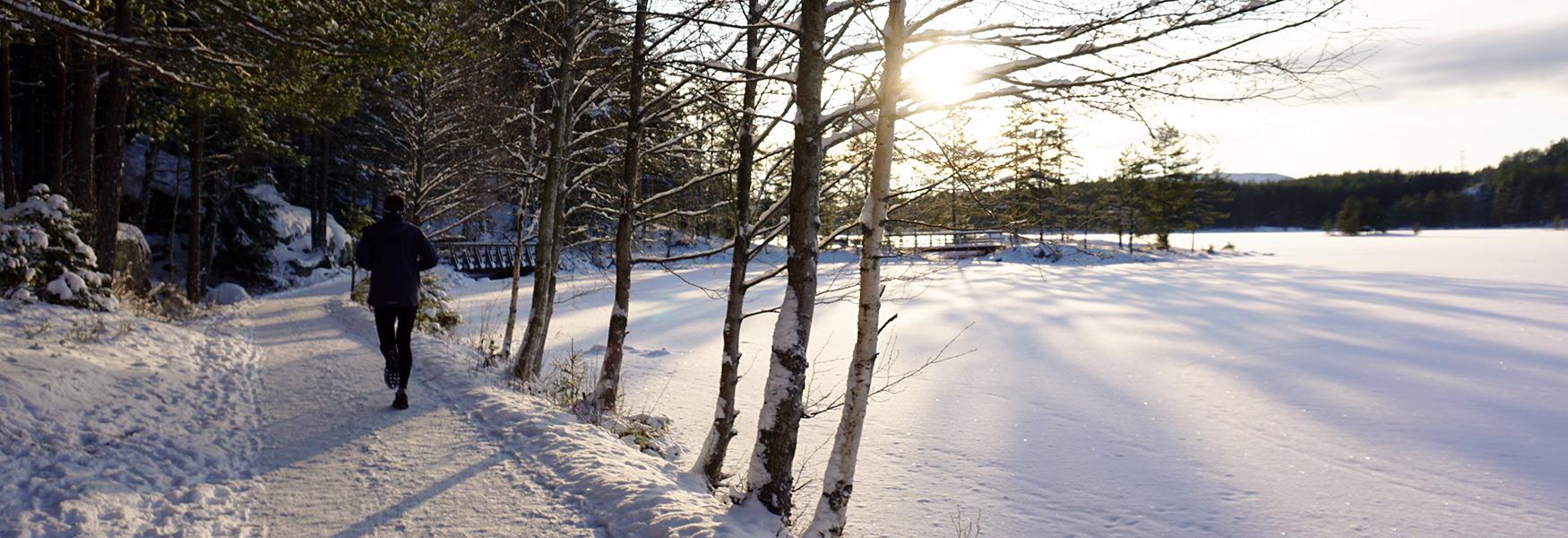 man som jogger langs et snødekket vann om vinteren